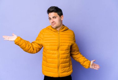 Mor arka planda izole edilmiş genç beyaz bir adam. Kafası karışmış ve omuz silkiyor. Kopya alanını tutmak için..