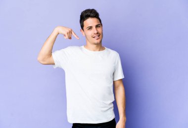 Mor arka planda izole olmuş genç beyaz bir adam gömlek fotokopisini elle gösteriyor, gururlu ve kendinden emin.