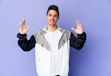 Mor arka planda izole edilmiş genç beyaz bir adam. Elinde işaret parmaklarıyla küçük bir şey tutuyor, gülümsüyor ve kendinden emin..