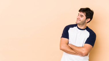 Bej arka planda izole edilmiş genç adam kollarını kavuşturarak gülümsüyor..