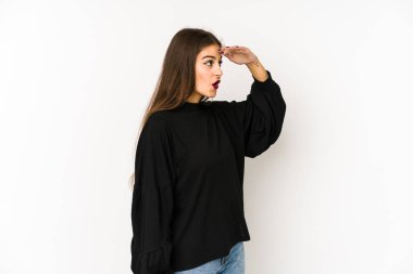 Beyaz arka planda soyutlanmış genç beyaz bir kadın çok uzaklara bakıyor ve elini alnına koyuyor..