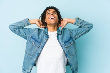 Genç siyah adam kot ceket giyiyor. Kendine güveniyor. Elleri başının arkasında..