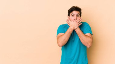 Bej arka planda izole edilmiş genç adam elleriyle ağzını kapatırken şok oldu..