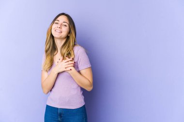Mor arka planda izole edilmiş beyaz bir kadın, dost canlısı bir ifadeye sahip, avuçlarını göğsüne bastırıyor. Aşk konsepti.