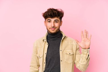 Arka planda poz veren genç bir Arap adam beş numarayı parmaklarıyla gülümsüyor..