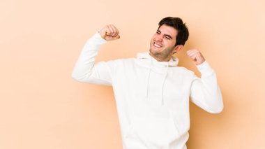 Genç adam bej arka planda izole edilmiş zafer sonrası yumruğunu kaldırıyor, kazanan konsept..