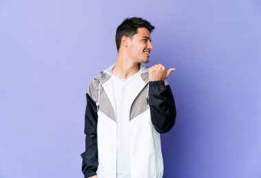 Mor arka plan noktalarında izole genç beyaz adam başparmak uzakta, gülüyor ve kaygısız.