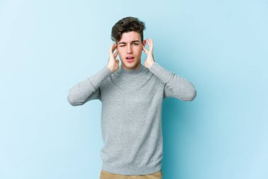 Genç beyaz adam mavi arka planda izole edilmiş parmaklarıyla kulaklarını kapatıyor, gürültülü bir ortam tarafından stresli ve umutsuz..