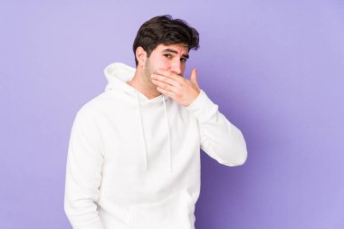 Mor arka planda izole edilmiş genç bir adam ağzını kapatıyor ve elleri endişeli görünüyor..