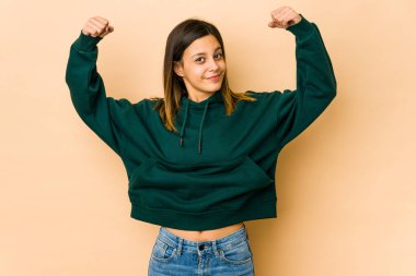 Bej arka planda izole edilmiş genç bir kadın. Güçlü bir jest yapıyor. Kadınsı gücün sembolü.