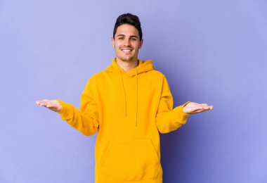 Mor arka planda izole genç beyaz adam kollarıyla ölçek yapar, mutlu ve kendinden emin hisseder..