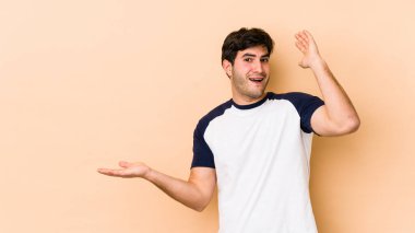 Bej arka planda izole edilmiş genç bir adam, bir avuç içinde fotokopi alanı tutuyor, el üstünde tutuyor. Şaşırmış ve mutlu..