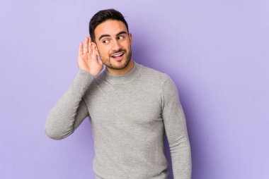 Mor arka planda izole edilmiş genç beyaz bir adam bir dedikoduyu dinlemeye çalışıyor..