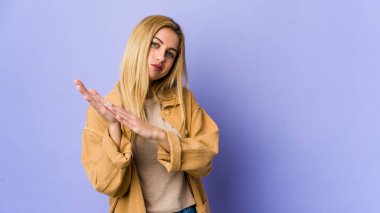 Mor arka planda soyutlanmış genç sarışın kadın enerjik ve rahat hissediyor, ellerini ovuşturuyor..