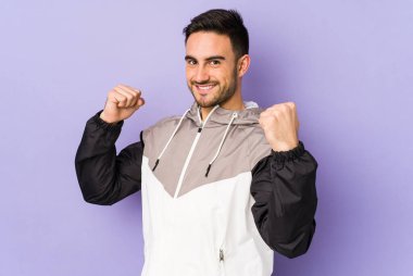 Mor arka planda izole edilmiş genç beyaz adam tasasız ve heyecanlı bir şekilde tezahürat yapıyor. Zafer konsepti.