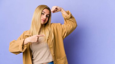 Mor arka planda izole edilmiş genç sarışın kadın güçlü bir hareket gösteriyor, kollarıyla, kadınsı gücün sembolü.