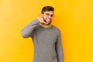 Sarı arka planda izole edilmiş genç beyaz adam parmaklarıyla bir cep telefonu hareketi gösteriyor..