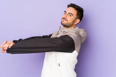Mor arka planda izole edilmiş genç beyaz adam kollarını uzatıyor, rahat pozisyonda..