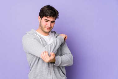 Genç adam mor arka planda izole edilmiş dirsek masajı yapıyor, kötü bir hareketin ardından acı çekiyor..