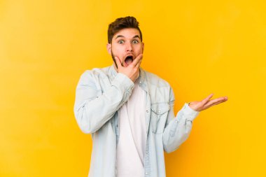 Sarı arka planda izole edilmiş genç beyaz bir adam bir avuç içinde fotokopi alanı tutuyor, el üstünde tutuyor. Şaşırmış ve mutlu..