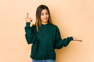 Bej arka planda izole edilmiş genç bir kadın elinde bir ürün tutuyor..