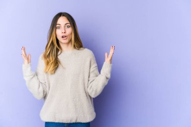 Mor arka planda izole genç beyaz kadın zaferi ya da başarıyı kutluyor, şaşırıyor ve şok oluyor..