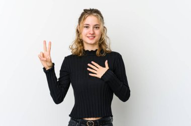 Beyaz arka planda genç beyaz kadın yemin ediyor, elini göğsüne koyuyor..