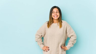 Mavi arka planda izole edilmiş genç bir kadın gülüyor ve gözlerini kapıyor, rahatlamış ve mutlu hissediyor..