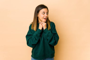 Bej arka planda izole edilmiş genç bir kadın şans için dua ediyor, şaşırmış ve ağzı açık bir şekilde önüne bakıyor..