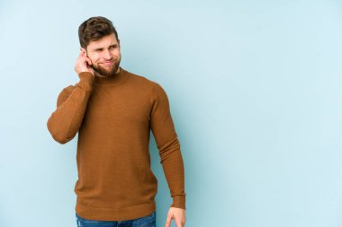Genç beyaz adam mavi arka planda izole edilmiş parmaklarıyla kulaklarını kapatıyor, gürültülü bir ortam tarafından stresli ve umutsuz..