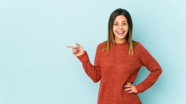 Mavi arka planda izole edilmiş genç bir kadın işaret parmağıyla işaret ederek gülümsüyor..