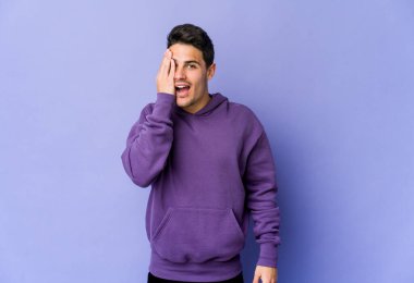 Mor arka planda izole edilmiş genç beyaz adam yüzünün yarısını palmiye ile kaplayarak eğleniyor..