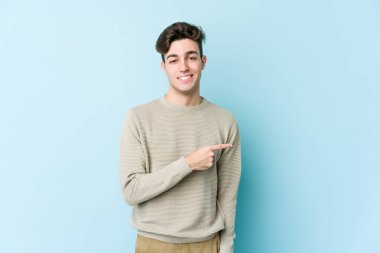 Mavi arka planda izole edilmiş genç beyaz adam gülümsüyor ve boş alanda bir şeyler gösteriyor..