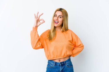 Beyaz arka planda izole edilmiş genç sarışın bir kadın bir göz kırptı ve elleriyle iyi bir jest yaptı..