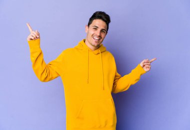 Mor arka planda izole edilmiş genç beyaz adam farklı kopya alanlarını gösteriyor, birini seçiyor, parmağıyla gösteriyor..