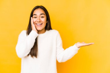 Sarı arka planda izole edilmiş genç bir kadın avuç içinde fotokopi alanı tutuyor, el üstünde tutuyor. Şaşırmış ve mutlu..