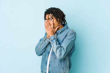 Kot ceket giyen genç siyahi adam parmaklarının arasından korkmuş ve gergin bir şekilde göz kırpıyor..