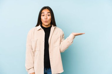 Mavi arka planda izole edilmiş genç bir kadın, avuç içinde kopya alanı bulundurmaktan etkilenmiş..