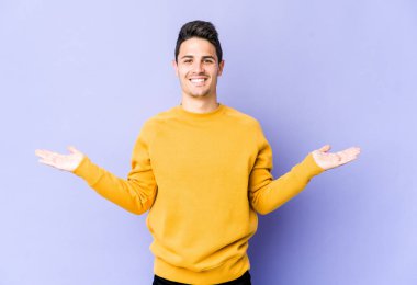 Mor arka planda izole genç beyaz adam kollarıyla ölçek yapar, mutlu ve kendinden emin hisseder..