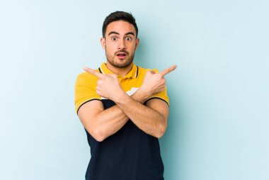 Mavi arka plan noktalarında izole genç beyaz adam, iki seçenek arasında seçim yapmaya çalışıyor.