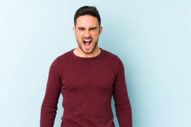 Kafkasyalı genç adam mavi arka planda izole edilmiş. Çok kızgın, öfkeli, hayal kırıklığına uğramış..