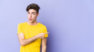 Mor arka planda izole edilmiş genç beyaz adam gülümsüyor ve boş alanda bir şeyler gösteriyor..