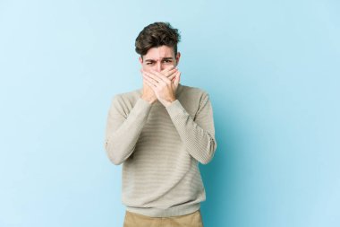 Kafkasyalı genç adam mavi arka planda izole edilmiş ağzı kapalı ve elleri endişeli görünüyor..