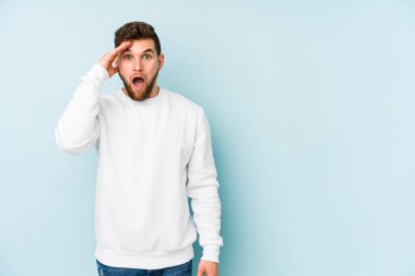 Mavi arka planda izole edilmiş genç beyaz adam yüksek sesle bağırıyor, gözleri açık ve elleri gergin tutuyor..