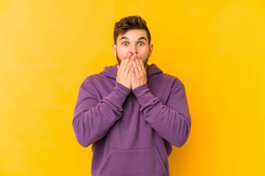 Sarı arka planda izole edilmiş genç beyaz adam şok olmuş, ağzı ellerle kaplanmış, yeni bir şey keşfetmeye hevesli..