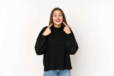 Beyaz arka planda izole edilmiş genç beyaz kadın gülümsüyor, parmaklarını ağıza doğrultuyor..