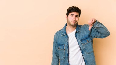 Bej arka planda izole edilmiş genç bir adam hoşlanmadığı bir jest gösteriyor, başparmakları aşağıda. Anlaşmazlık konsepti.