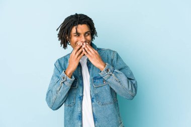 Kot ceket giyen genç siyah bir adam bir şeye gülüyor, elleriyle ağzını kapatıyor..