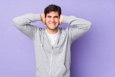 Mor arka planda izole edilmiş genç bir adam kulakları elleriyle kapatıyor ve yüksek sesli sesler duymamaya çalışıyor..