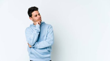 Beyaz arka planda izole edilmiş genç beyaz bir adam şüpheli ve şüpheci bir ifadeyle yana bakıyor..